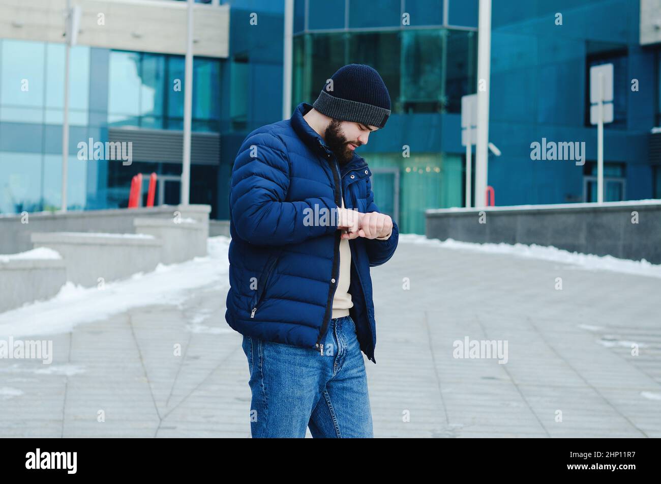 young elegant business man in winter casual clothes, jacket, hat. Walking in the city street, talking on the phone, making selfie. Working outdoor. Stock Photo