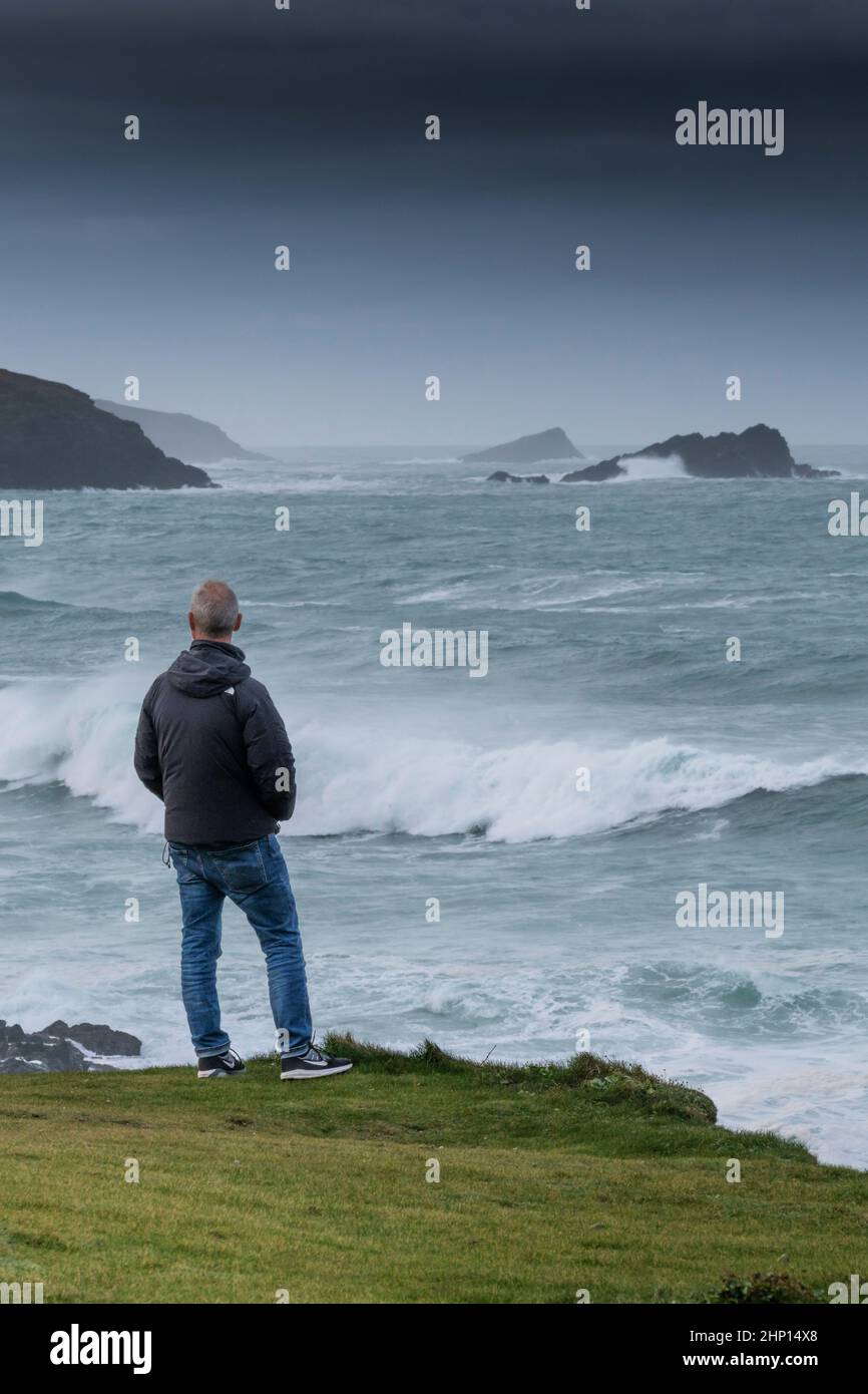 A man standing on the coast path looking out at the wild weather and rough sea in Fistral Bay in Newquay in Cornwall. Stock Photo