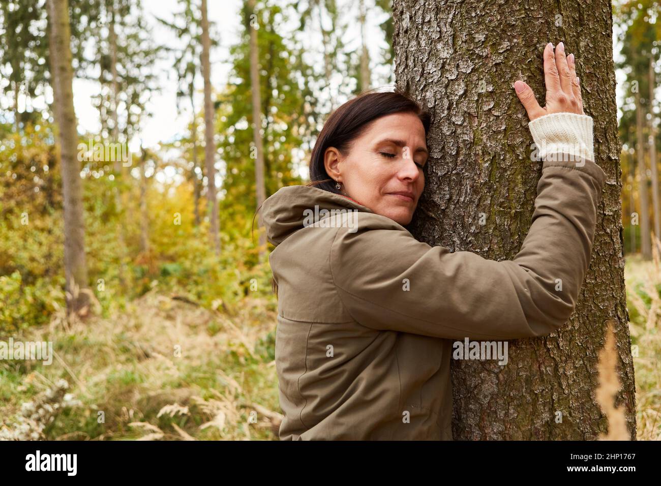 Woman in the forest hugs a tree with closed eyes for harmony and health Stock Photo