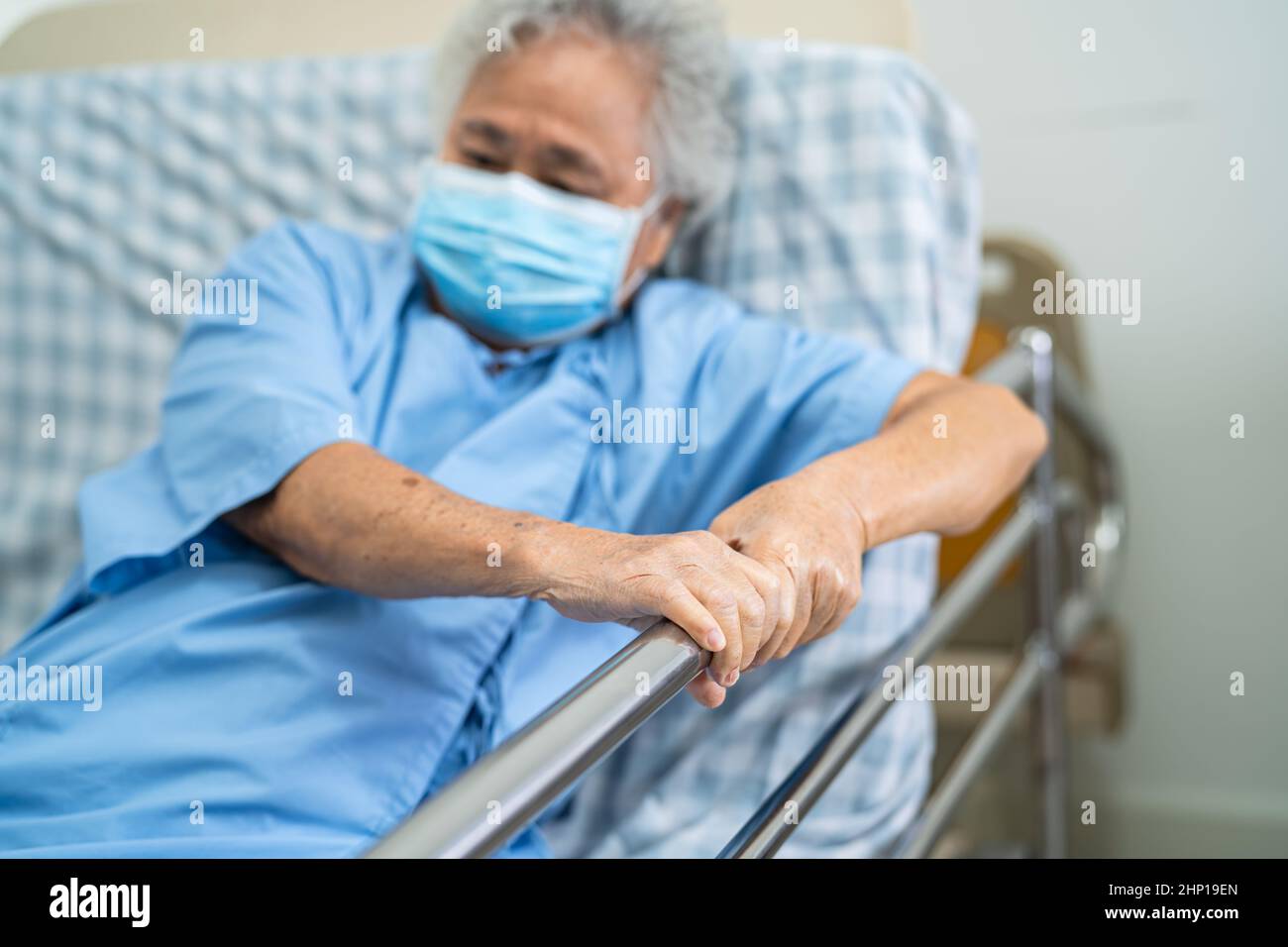 Asian senior or elderly old woman patient wearing mask for protect coronavirus lie down handle the rail bed with hope on a bed in the hospital Stock Photo