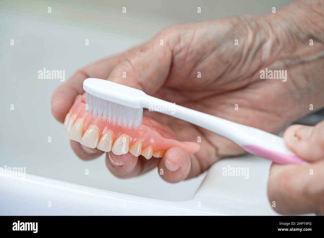 Asian senior or elderly old woman patient use toothbrush to clean partial denture of replacement
