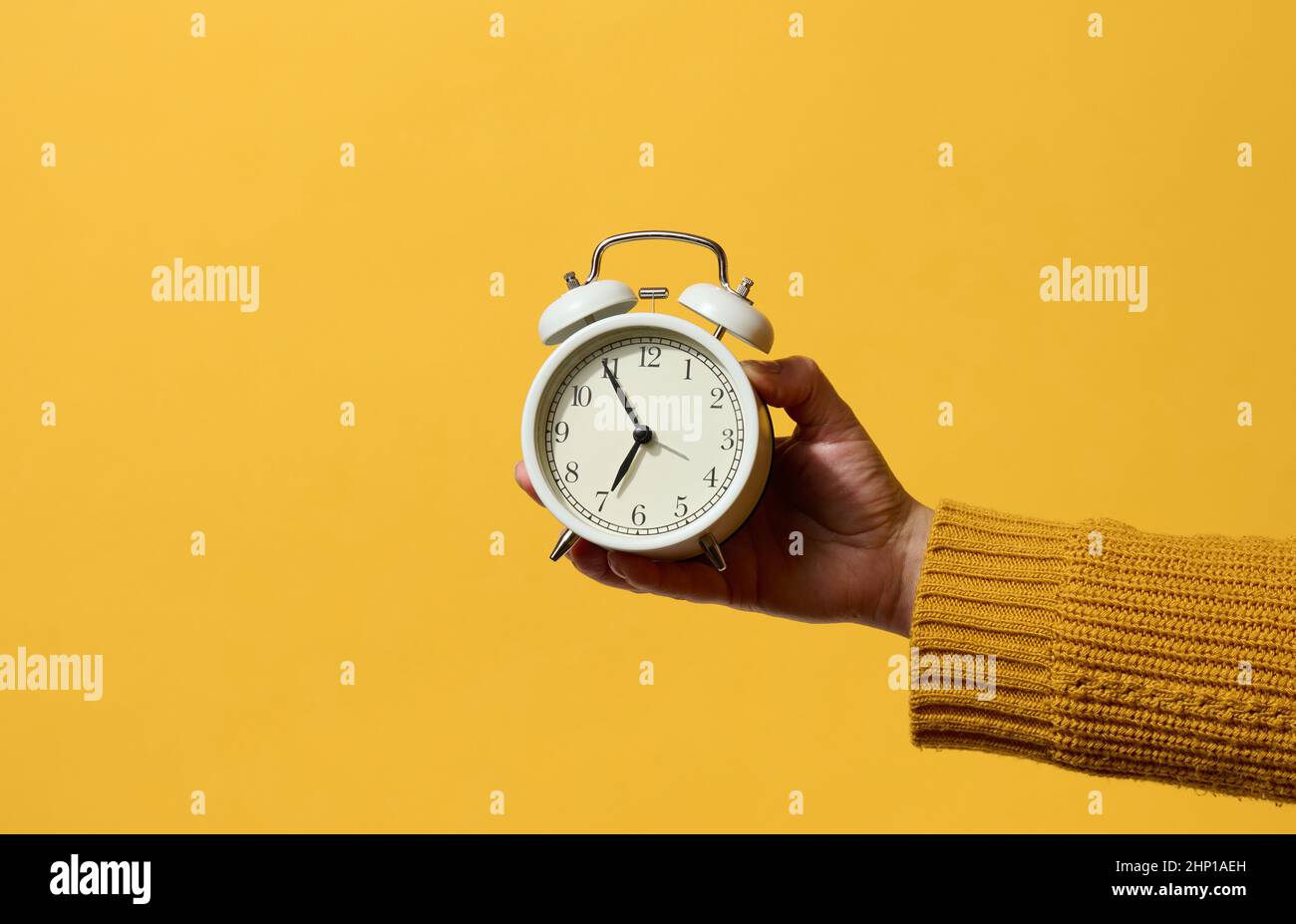 round alarm clock in a woman's hand, the time is five minutes to seven