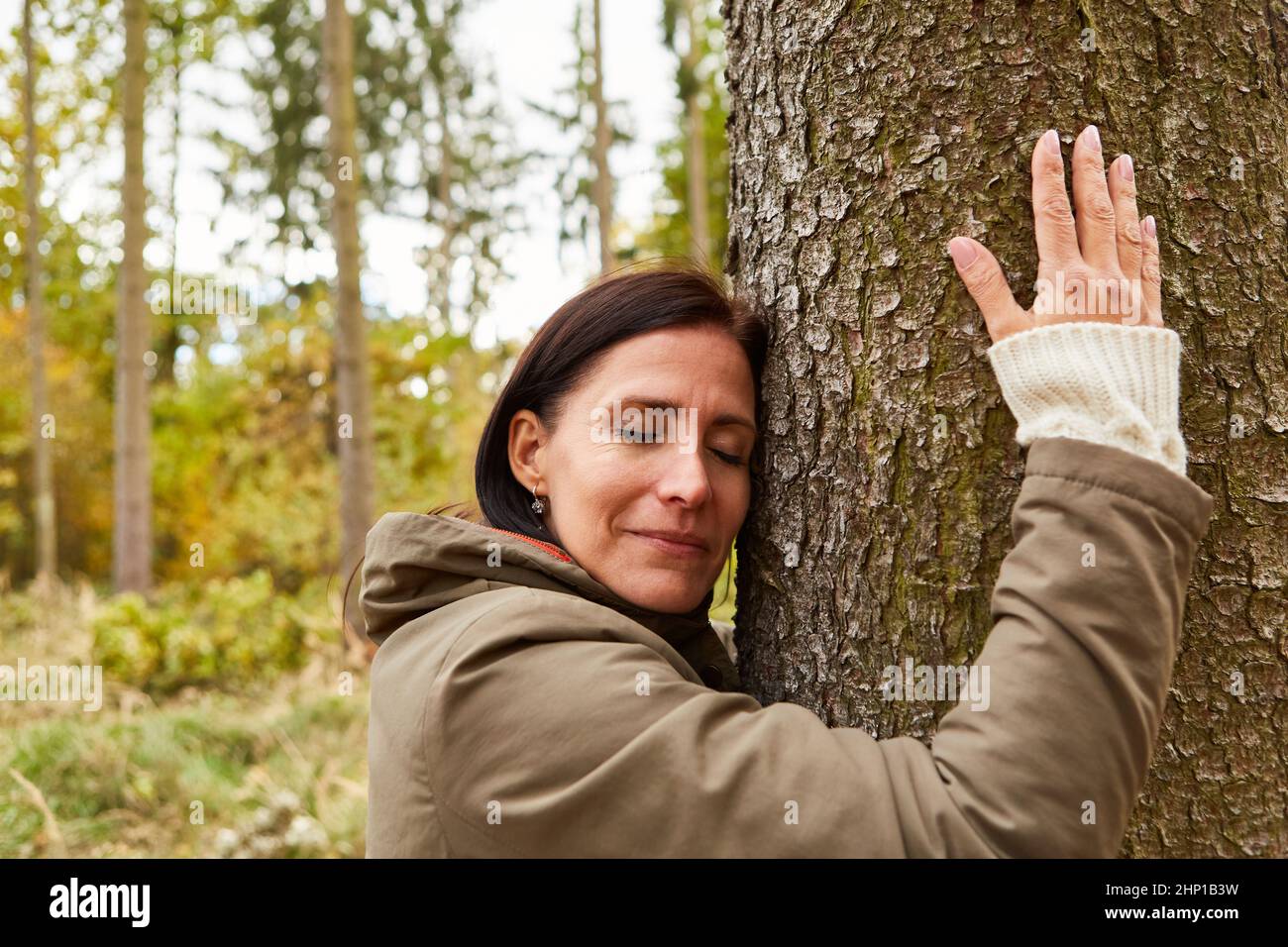 Woman hugging a tree with eyes closed during forest bathing for rest and relaxation Stock Photo