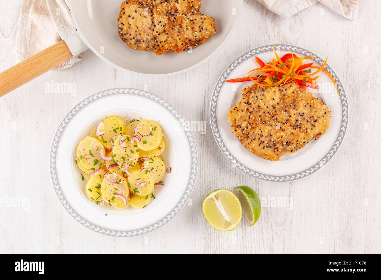 Crispy weiner schnitzel with sesame seeds on pan with potato salad from above. Chicken fried