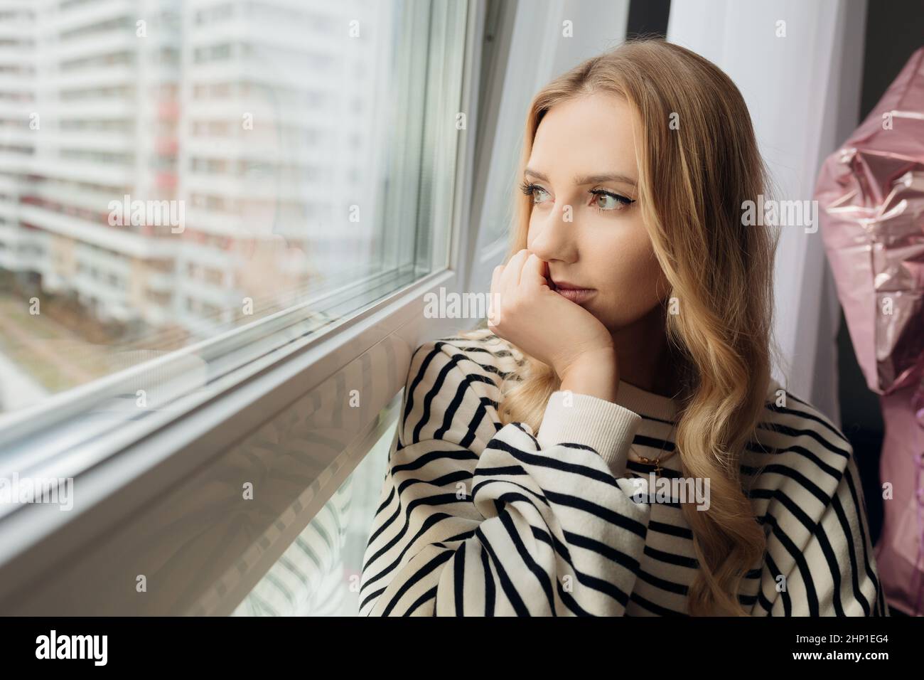 Portrait pensive blond pretty sad depressed woman on windowsill, looking distance. Lonely, tired, isolation. Close up Stock Photo