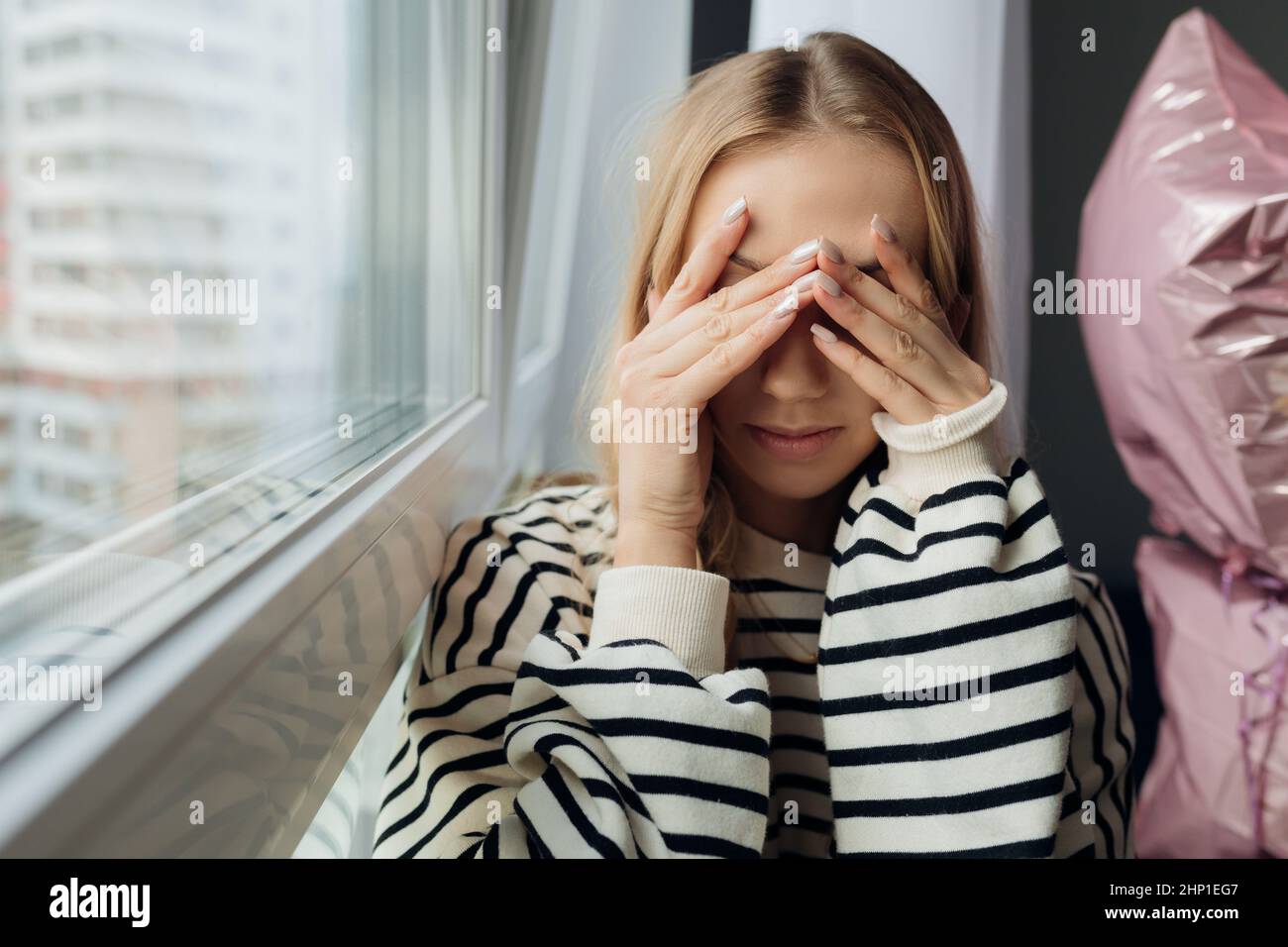 Portrait of pensive thoughtful blond pretty sad, upset, depressed woman sit on window sill, face hand. Violence bullying Stock Photo