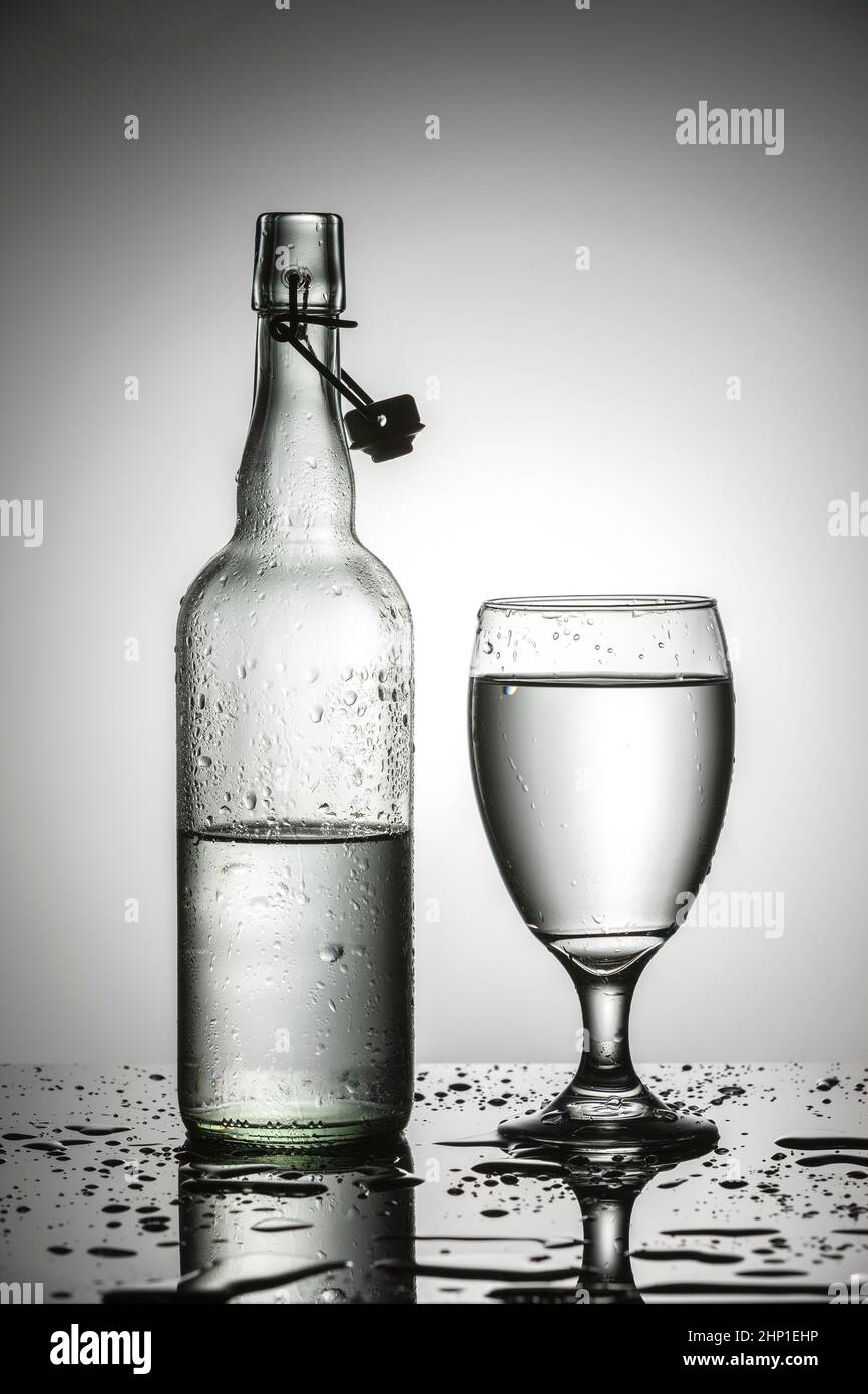 A studio photo of water in a glass next to a glass water bottle Stock