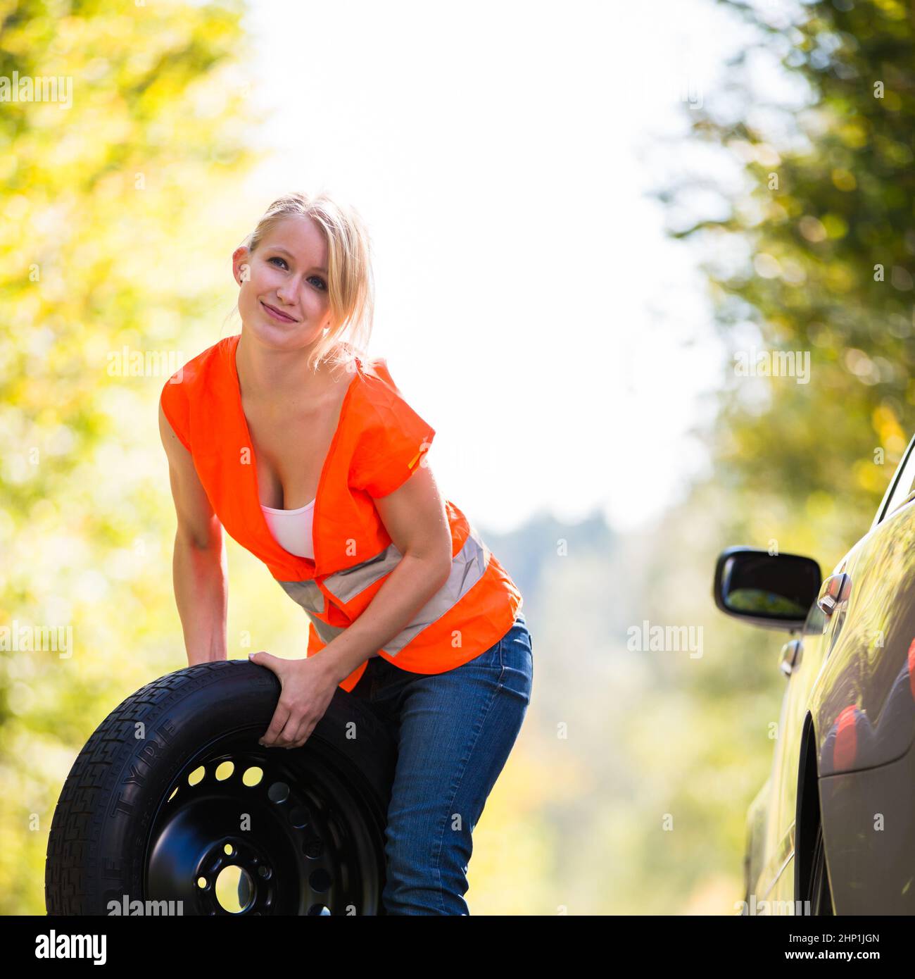 Young female driver wearing a high visibility vest, calling the roadside service/assistance after her car has broken down Stock Photo
