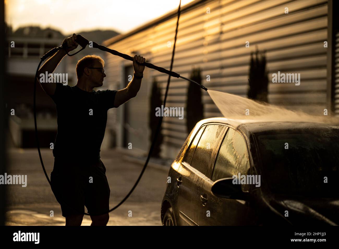 Young man washing his beloved car carefully in a manual car wash to