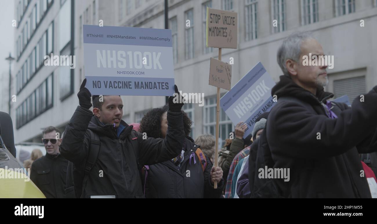 London, UK - 01 22 2022:  A young man holding a sign, ‘NHS100K, No Vaccine Mandate’, whilst marching with a crowd of protesters at Portland Place. Stock Photo