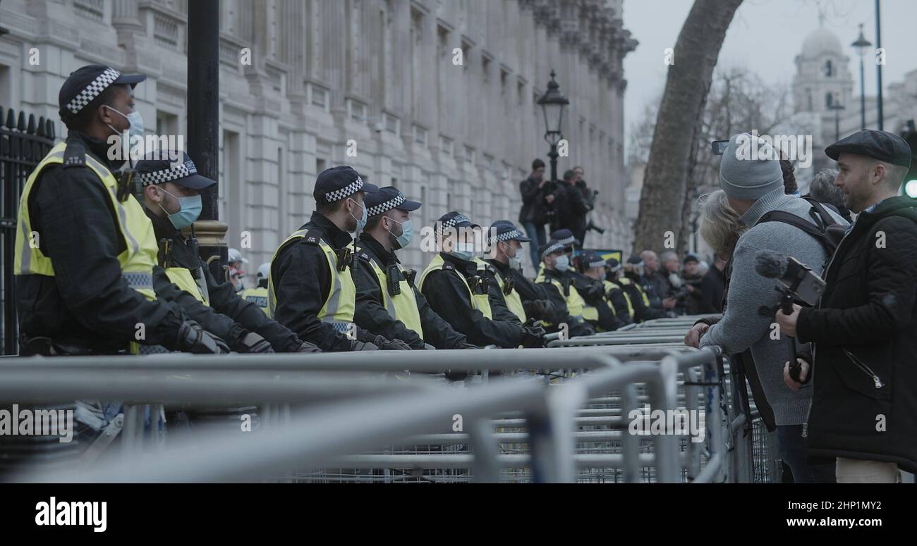 London, UK - 01 22 2022:  Police officers wearing face masks standing in line on Whitehall road, with a crowd of protesters in support of NHS100K. Stock Photo