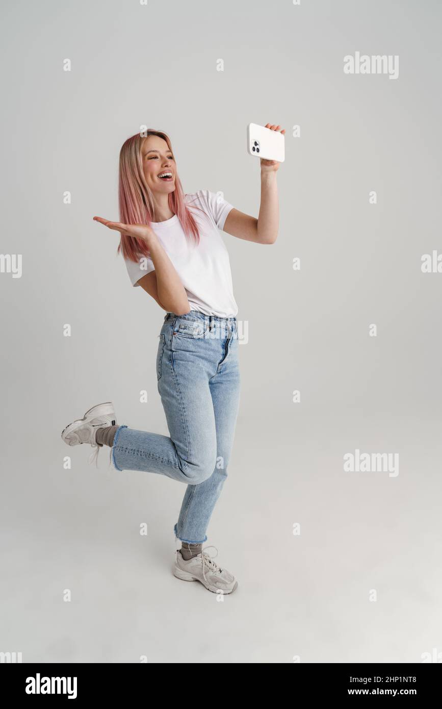 Happy young woman in casual wear jumping taking selfie holding mobile ...