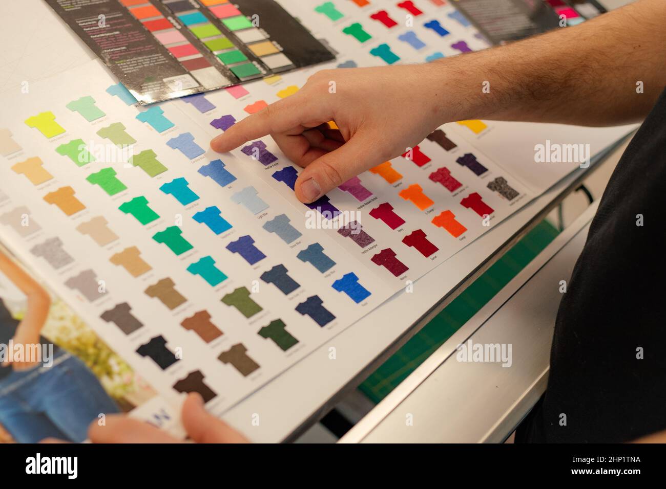 Cropped man hand choosing samples catalog multicolor advertising T-shirts palette film membrane. Textile production Stock Photo
