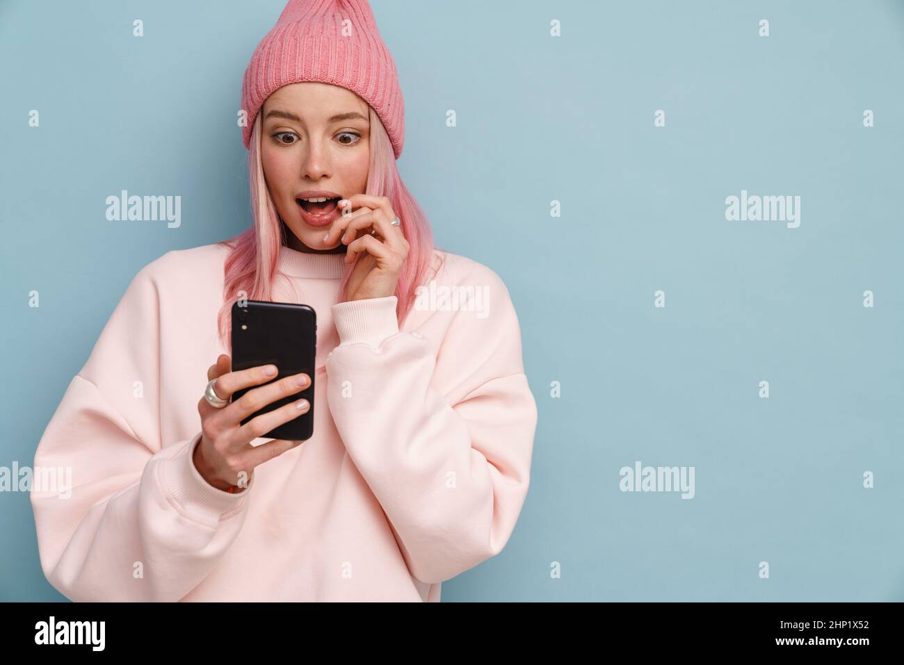 Young white woman expressing surprise while using mobile phone isolated over blue wall Stock Photo
