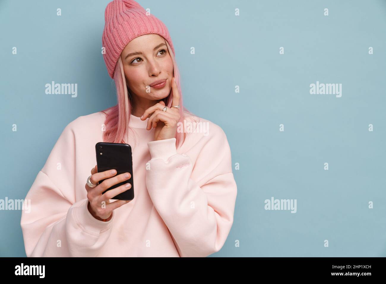 Young white woman looking aside while using mobile phone isolated over blue wall Stock Photo