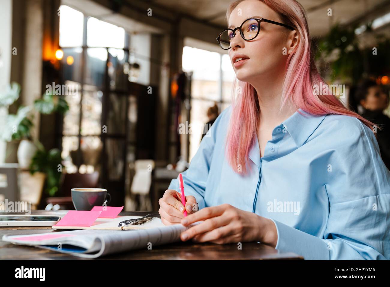 Young beautiful woman with pink hair studying and making notes while sitting in cafe Stock Photo