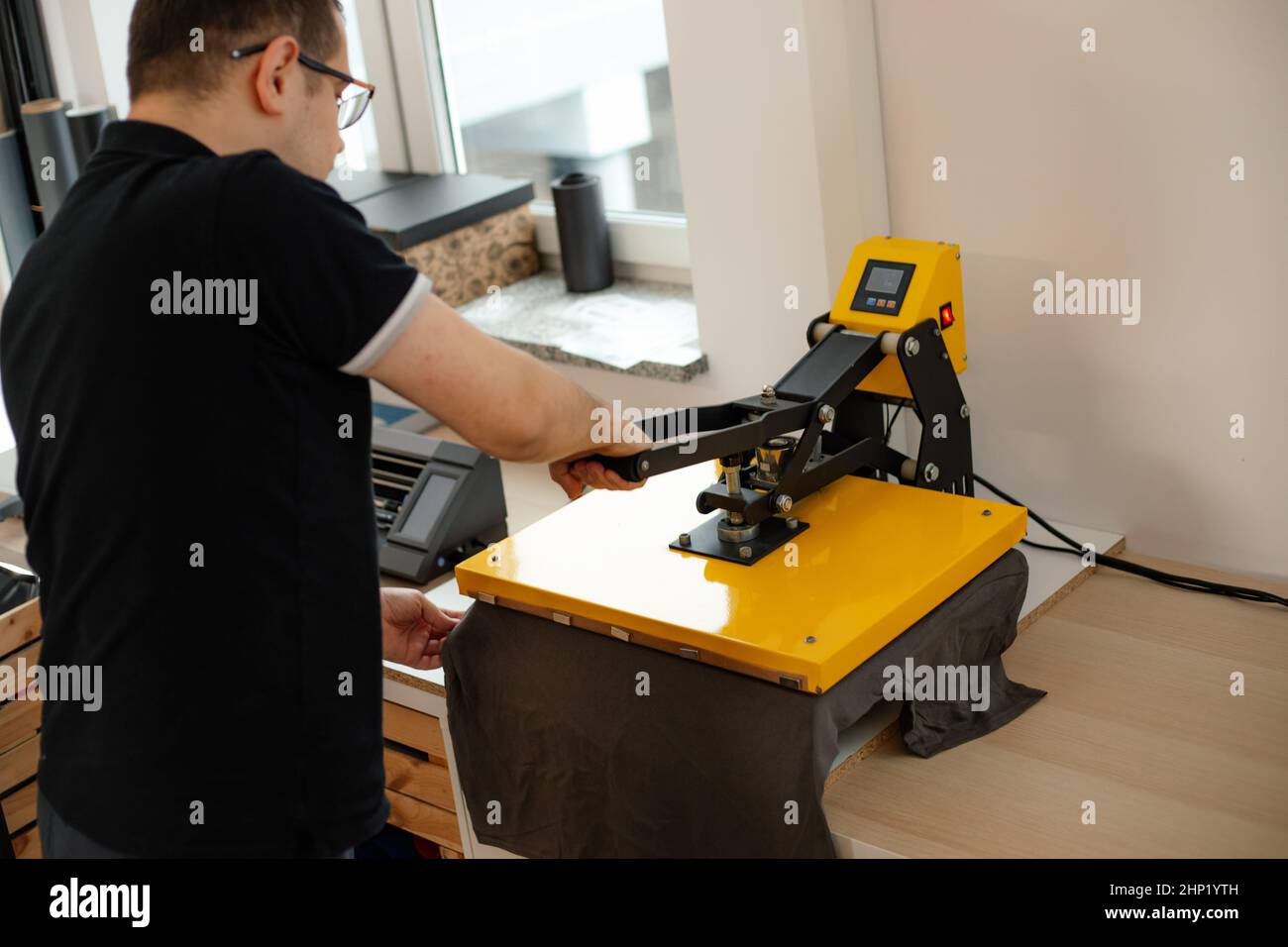 Man worker glasses back using heat thermal textile application transfer machine. Printing application T-shirt art design Stock Photo