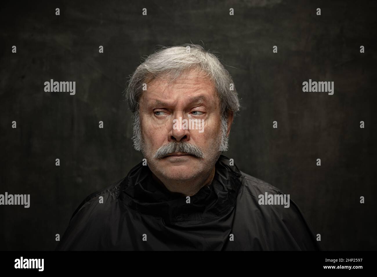 Portrait of seriuos senior man looking at camera isolated on dark vintage background. Concept of emotions, fashion, beauty, self-reinvention Stock Photo