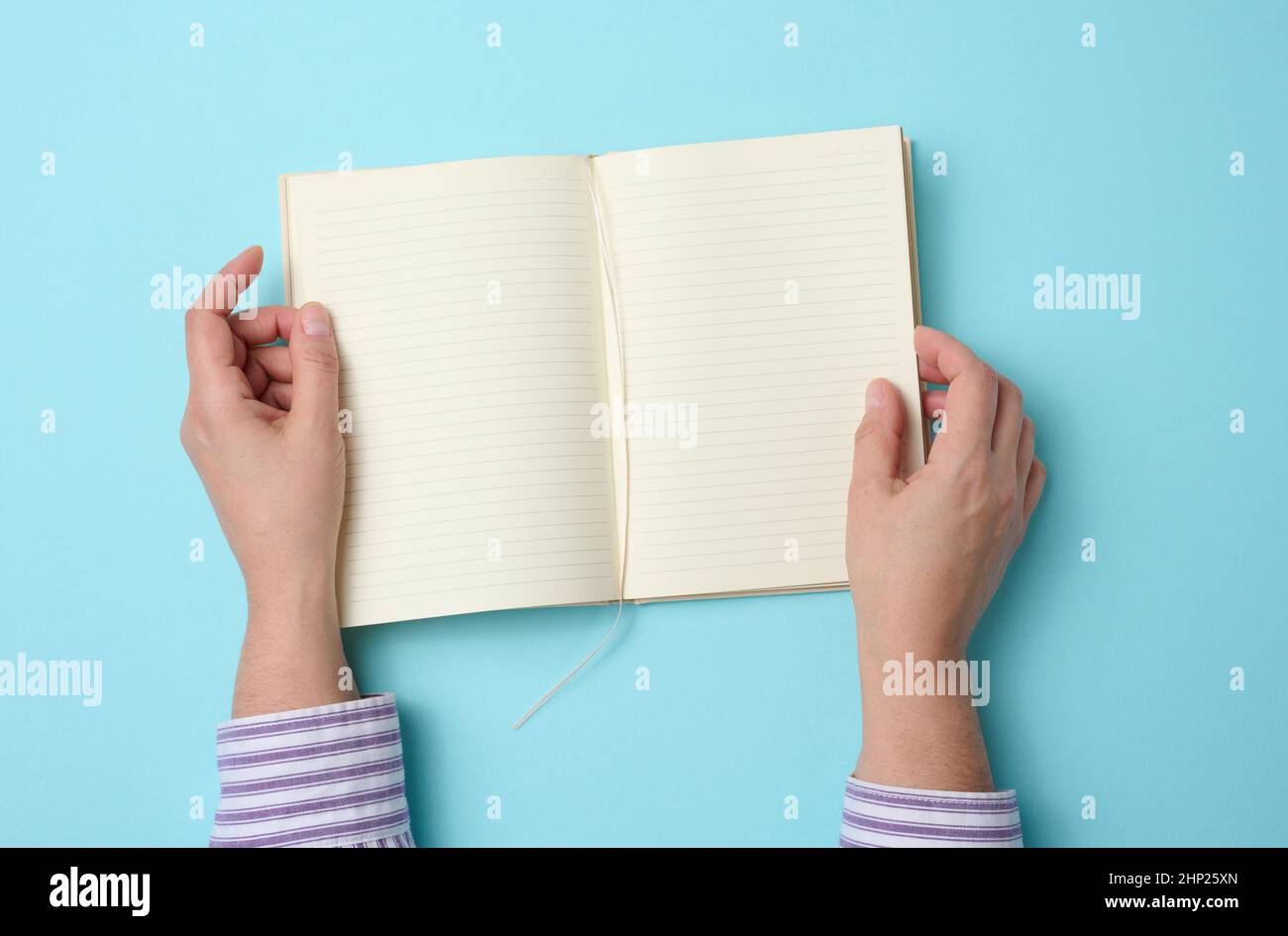 two female hands hold an open notebook with blank white sheets on a blue background, top view Stock Photo