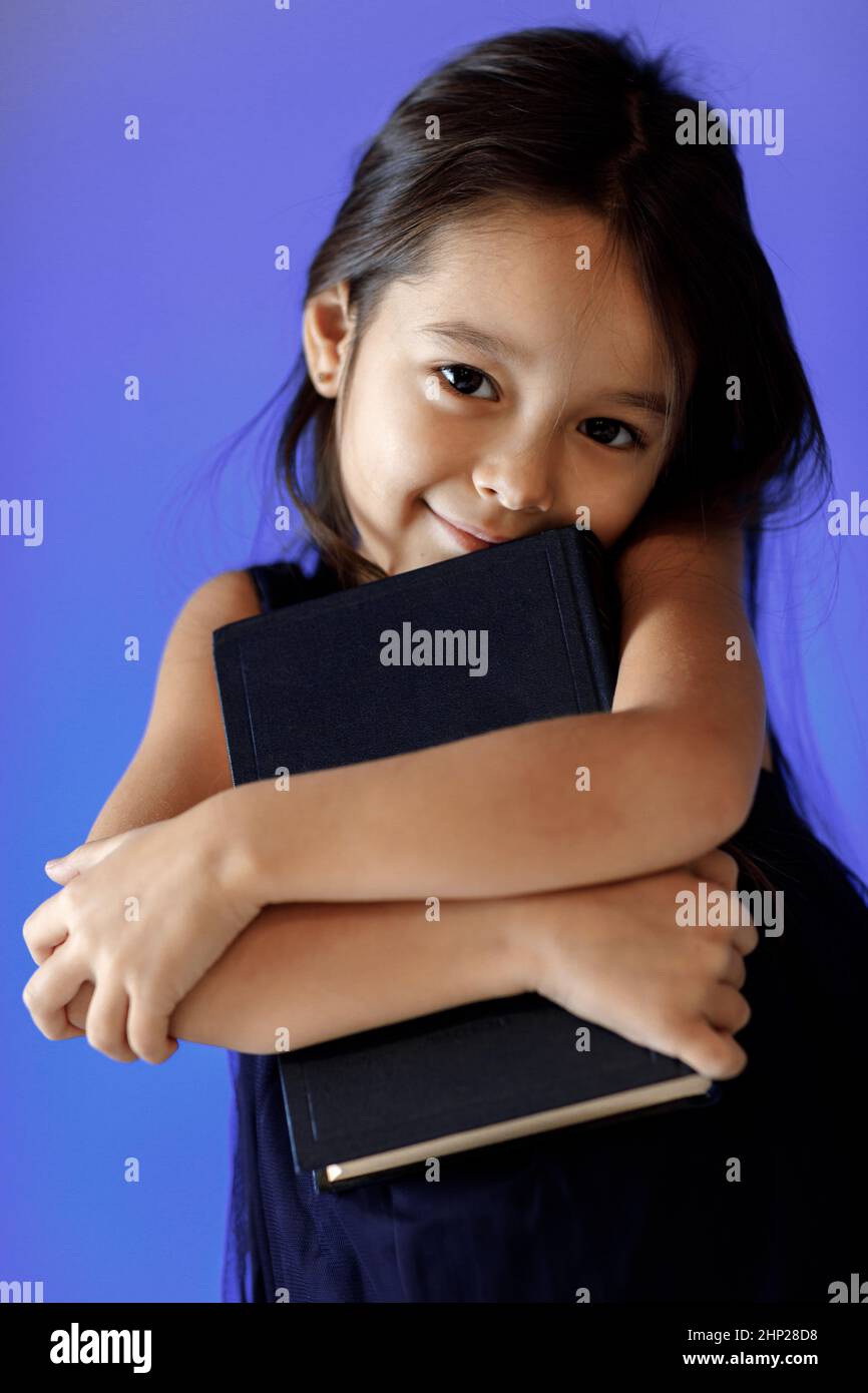 portrait of cute little girl in dark blue dress is reading a book ...