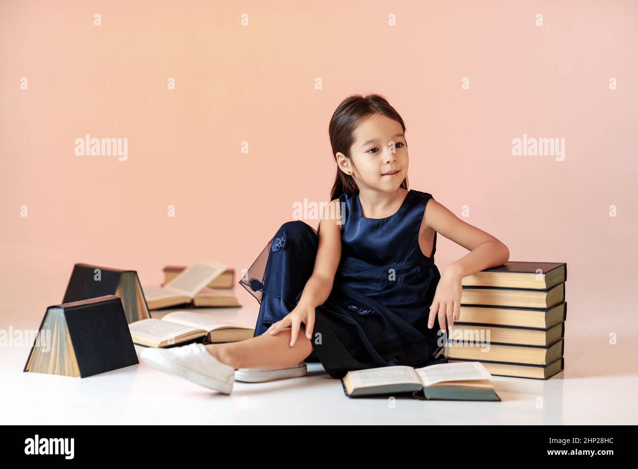 cute little girl in dark blue dress is reading a book. child and a lot ...