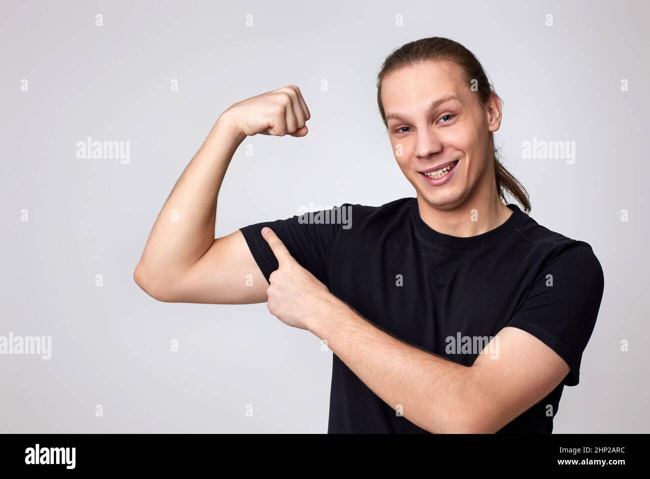 young fitness strong man show biceps muscles on hand isolated on gray background. Stock Photo