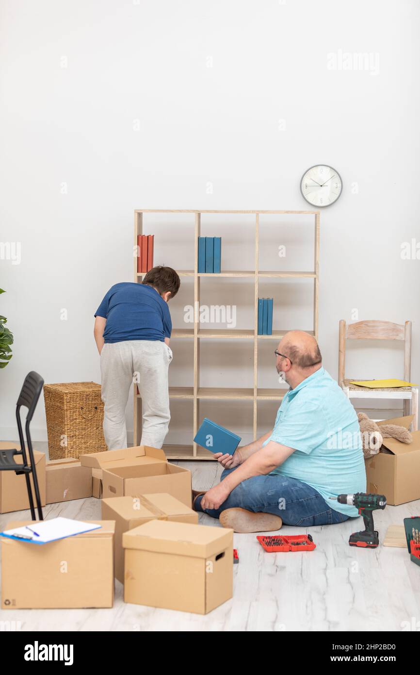 Dad and son arrange books on a bookcase immediately after moving Stock