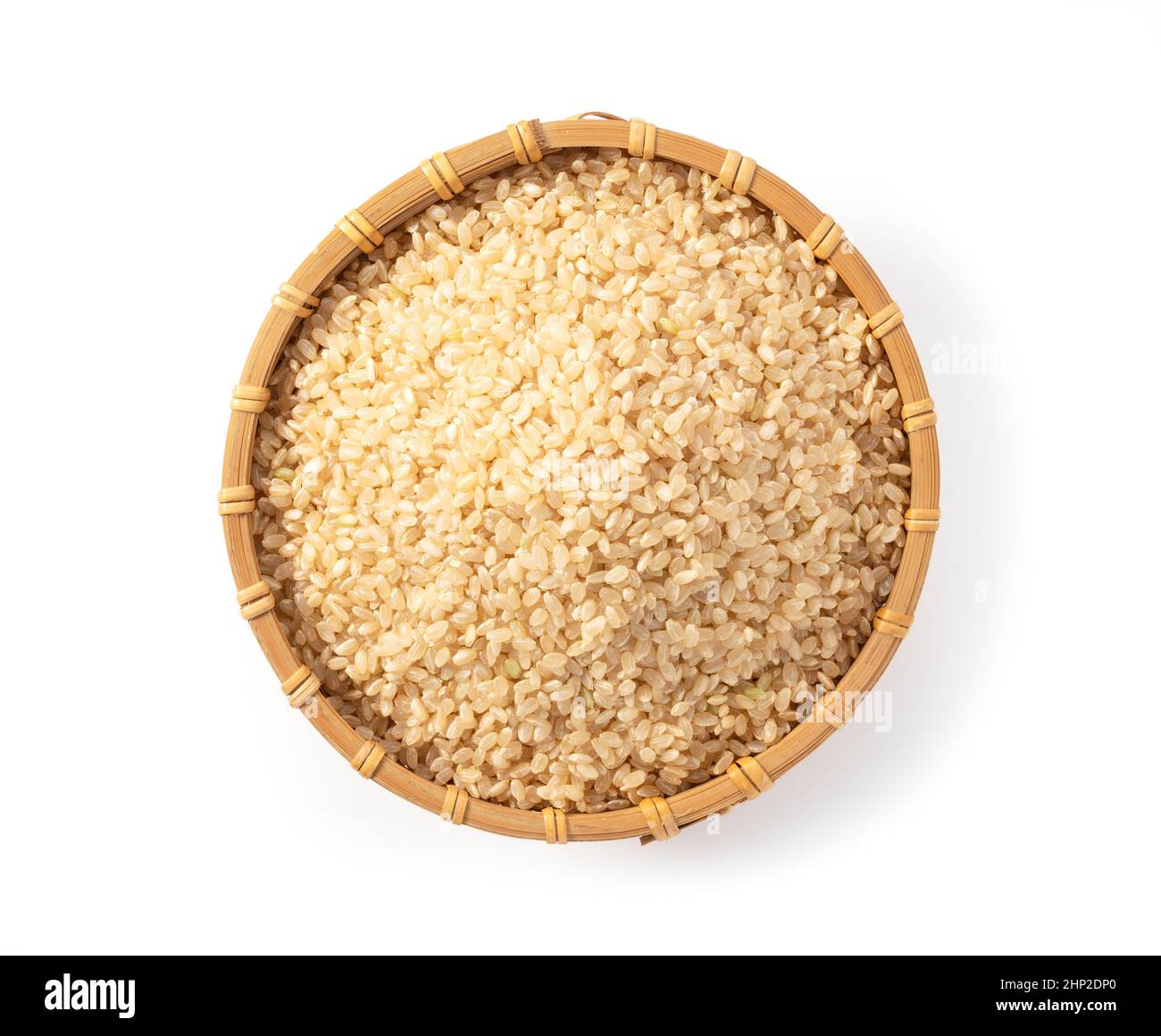 Brown rice in a bamboo colander set against a white background. A pile ...