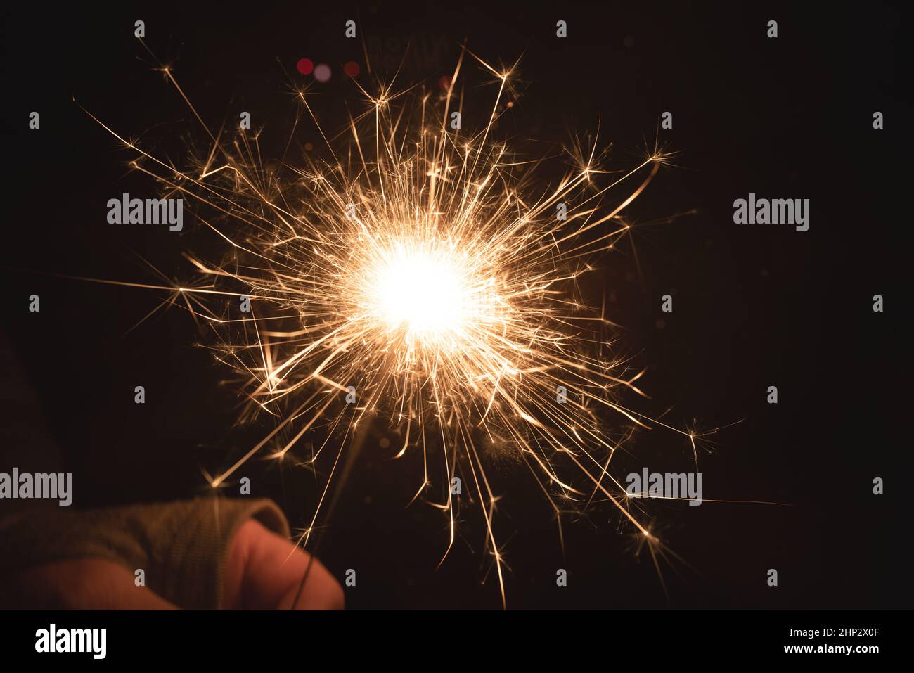 Burning sparkler at night. Hand holds a burning sparkler at night. Christmas background with colorful bokeh and space for text. Stock Photo