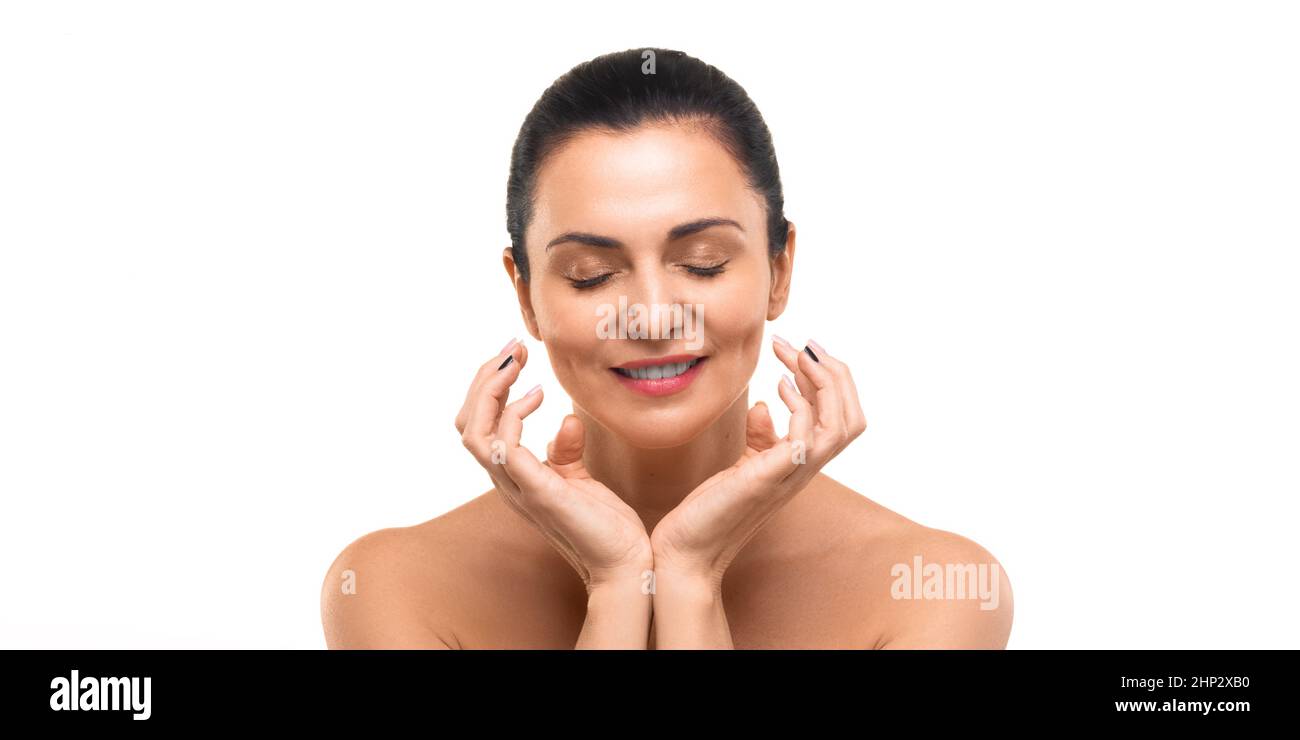 Portrait of a 40 years old woman with closed eyes and clean skin natural gentle refreshing makeup isolated on white background. Woman touching her ski Stock Photo