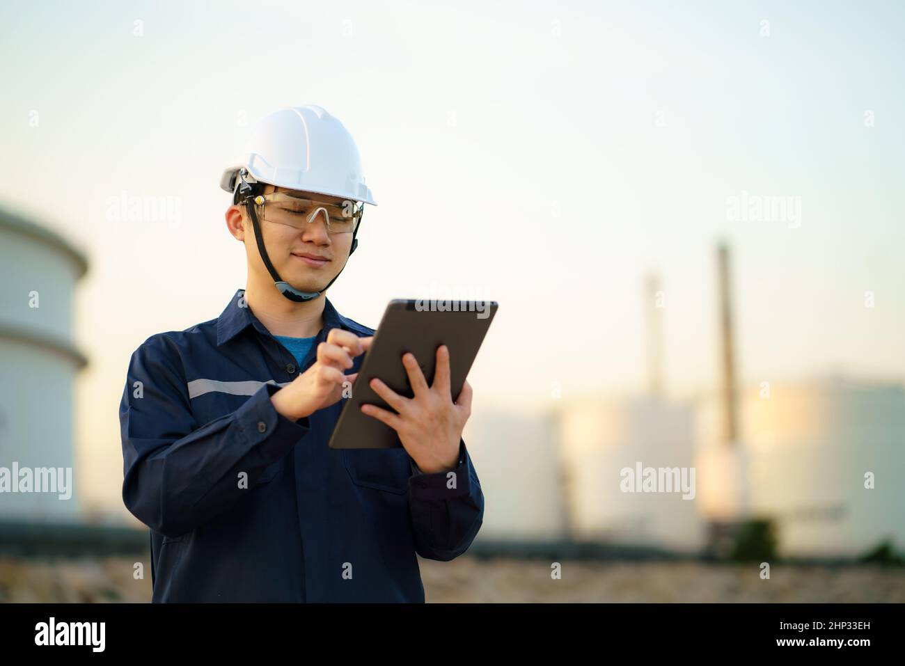 Asian engineer man are checking the maintenance of the oil refinery factory at evening via digital tablets. Stock Photo
