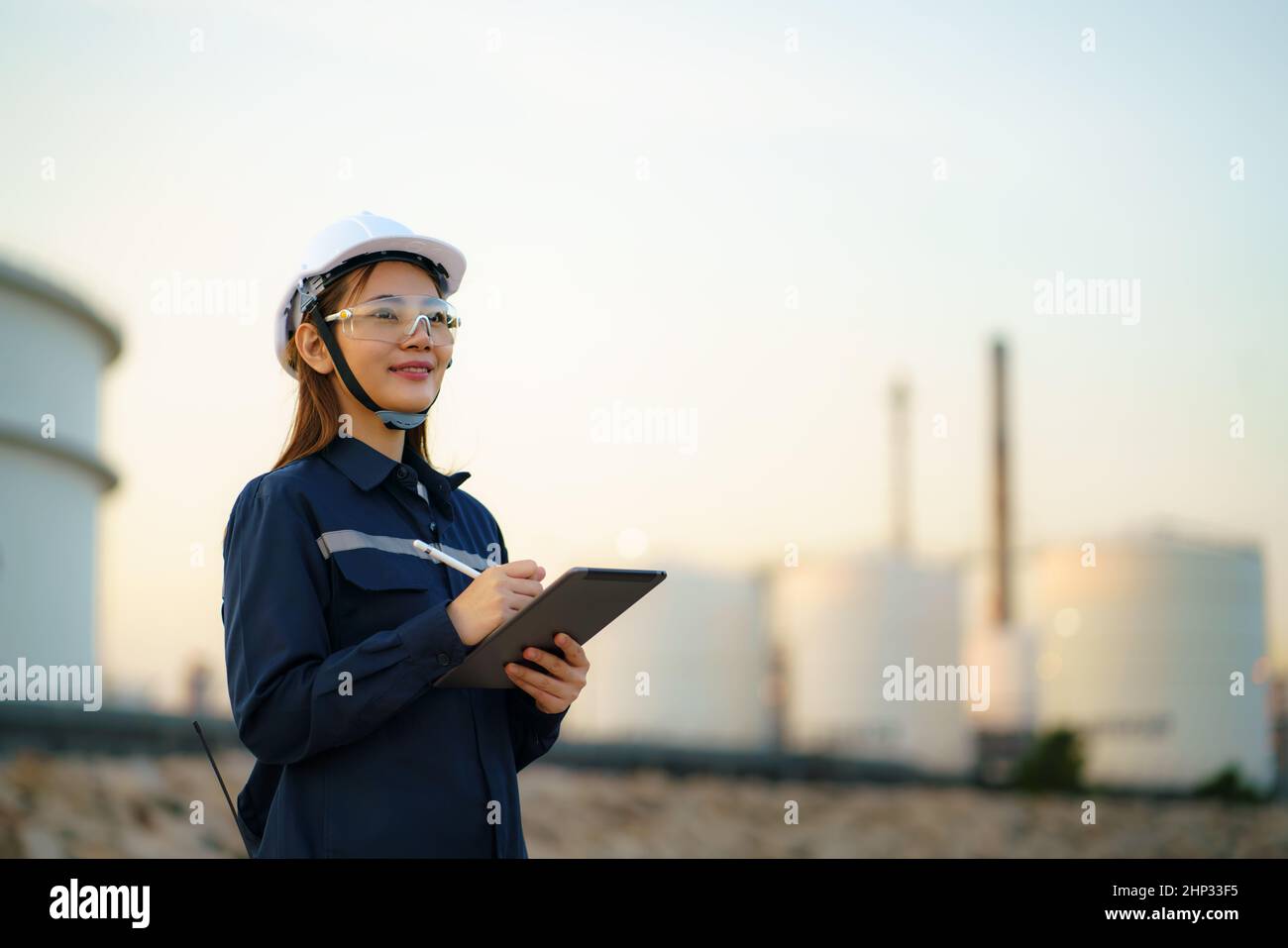 Asian woman petrochemical engineer working with digital tablet Inside oil and gas refinery plant industry factory at night for inspector safety qualit Stock Photo