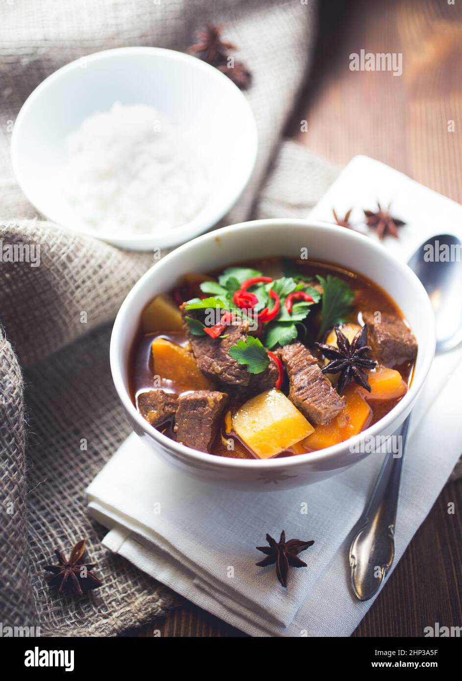 A bowl of vietnamese beef stew with potatoes and garnishes on a white