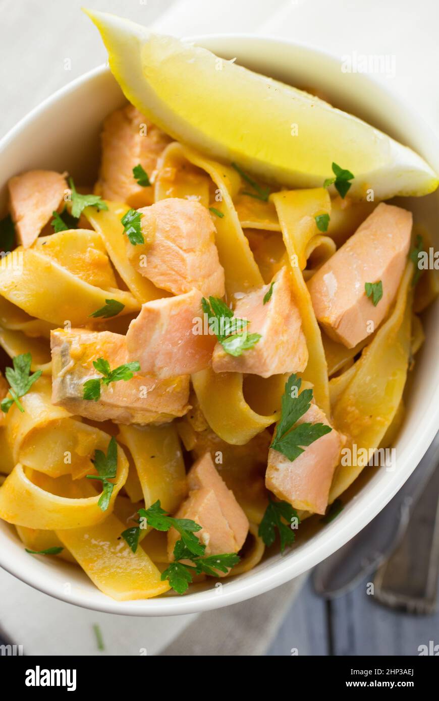 Italian salmon and lemon tagliatelle pasta in a white bowl served with a lemon wedge and parsley