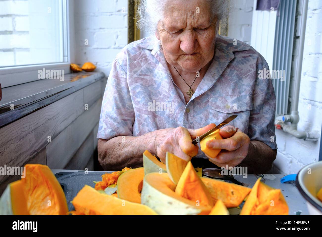 Old woman cuts and pills yellow pumpkin, cooking pumpkin soup, retirement life, selective focus Stock Photo