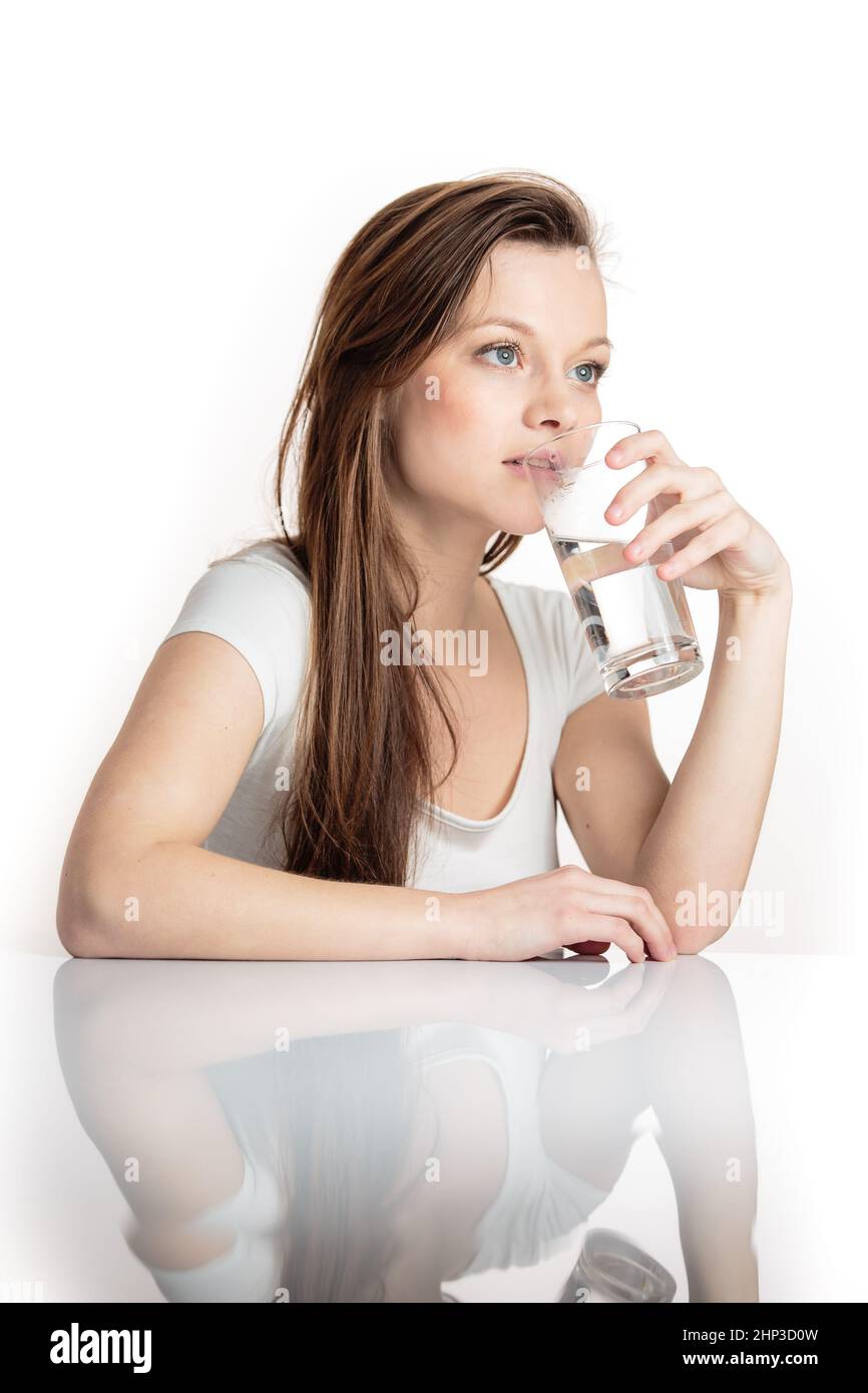 Pretty, young woman in her modern, clean and bright kitchen, pouring herself and drinking a glass of cold tap water(color toned imagey; shallow DOF) Stock Photo