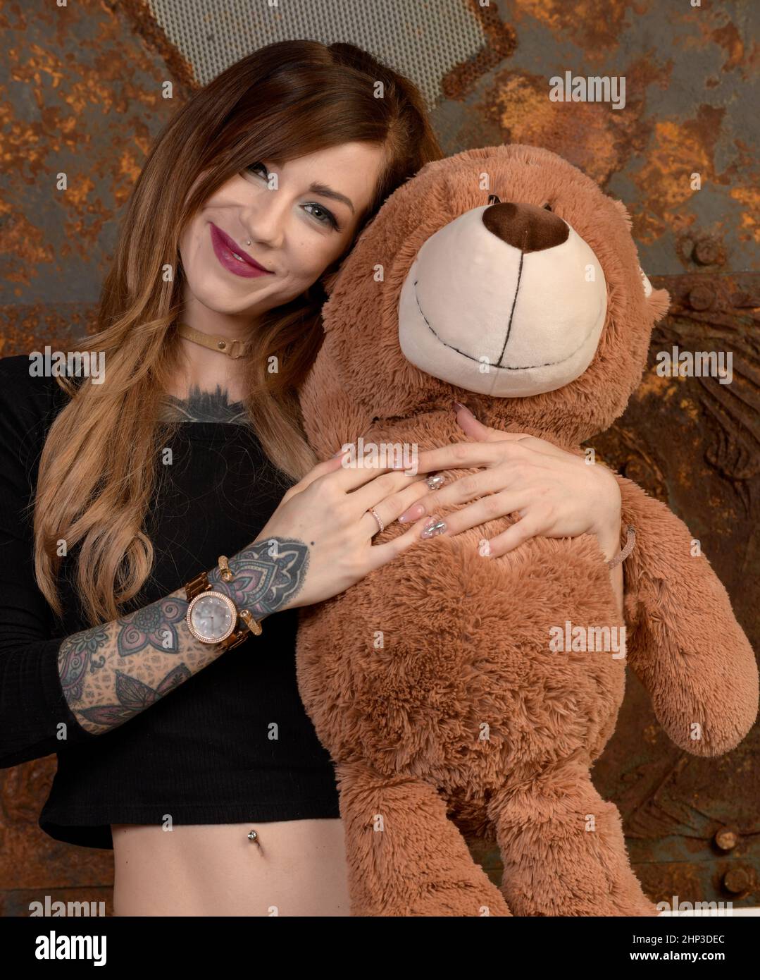 A pretty young tattooed woman stands by the open cain and hugs her huge ...