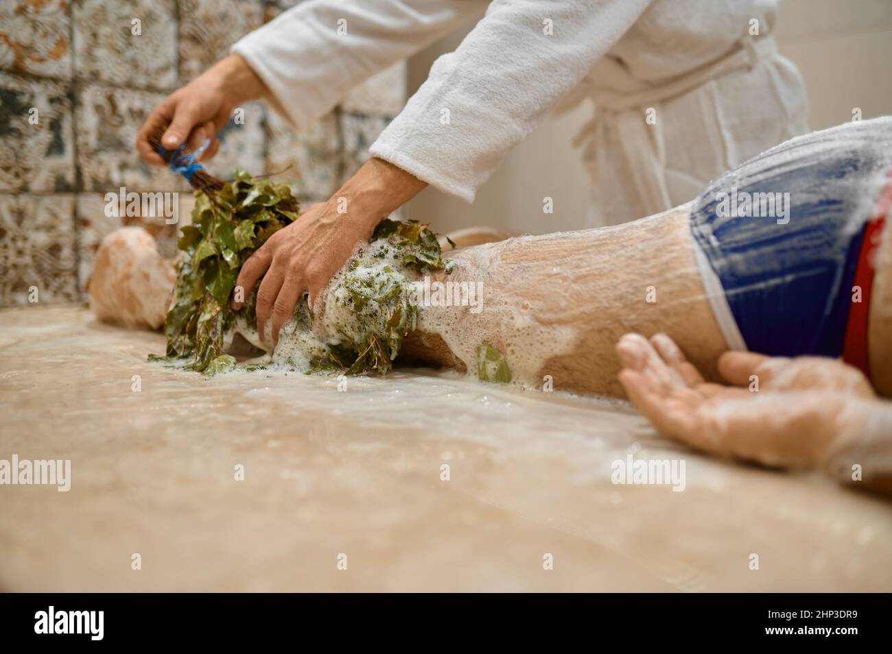 Man getting legs massage with oak broom in bath. Spa, hammam or russian