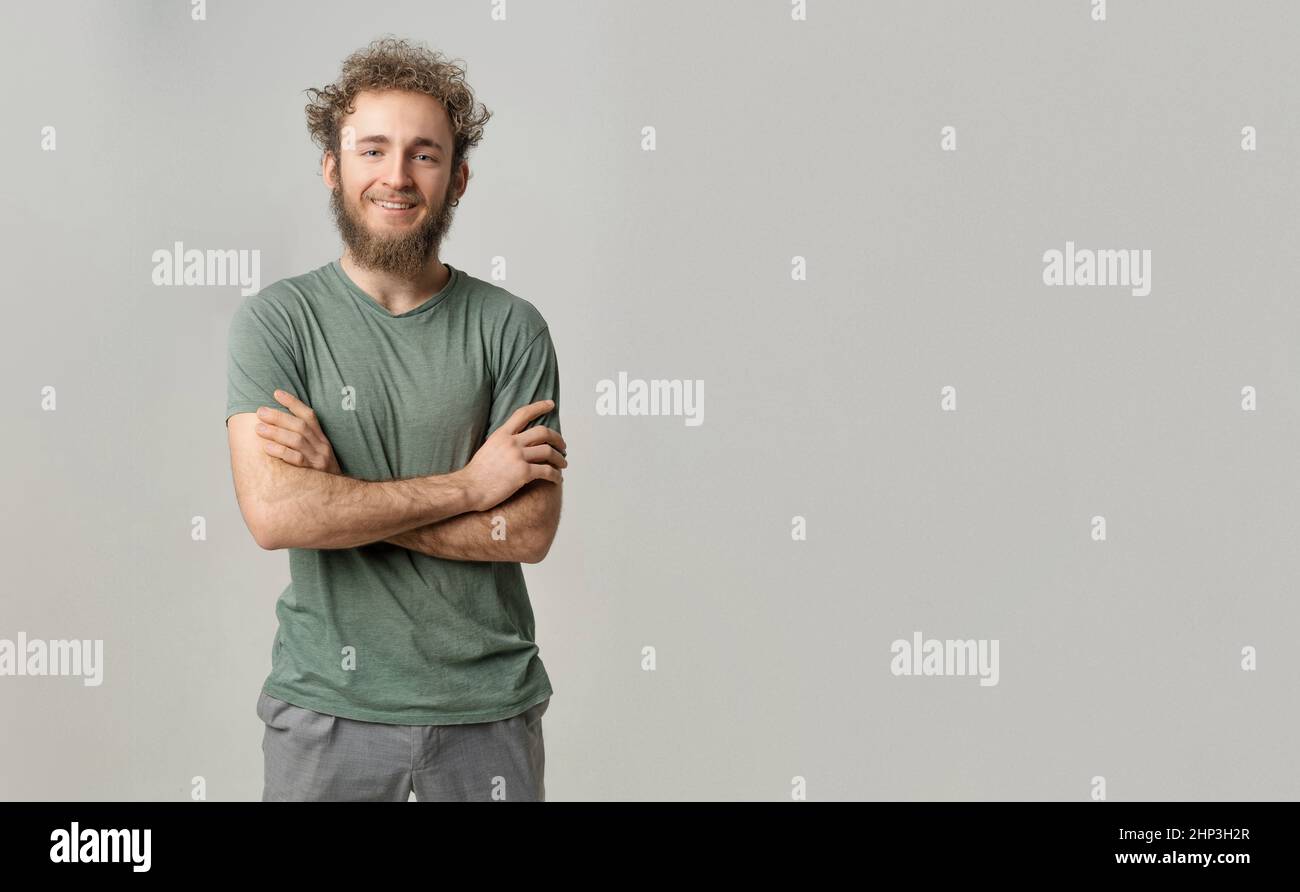 Handsome smiling young handsome bearded wild curly hair man with bright blue eyes isolated on white background. Young thinking man in green tshirt on white background.  Stock Photo