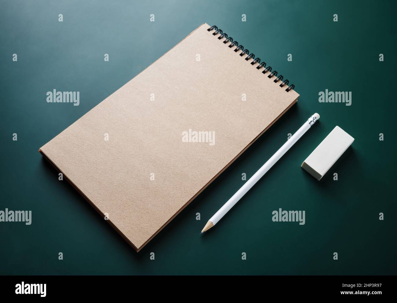 Photo of blank kraft sketchbook, pencil and eraser on green background