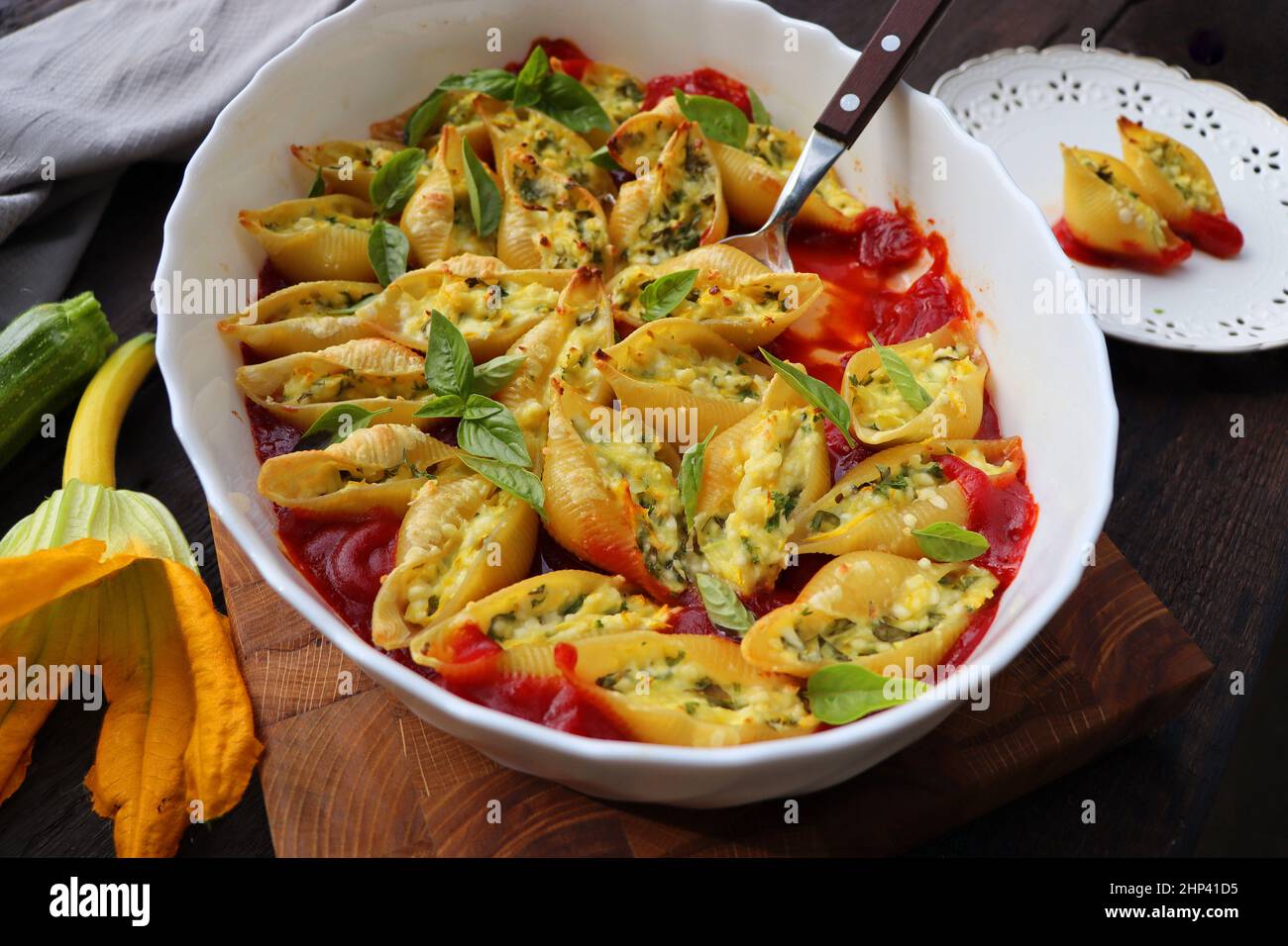 Big shell shape pasta stuffed with creamy soft cheese, zucchini and spinach sprinkled with parmesan cheese in baking dish wooden table, healthy dinner Stock Photo