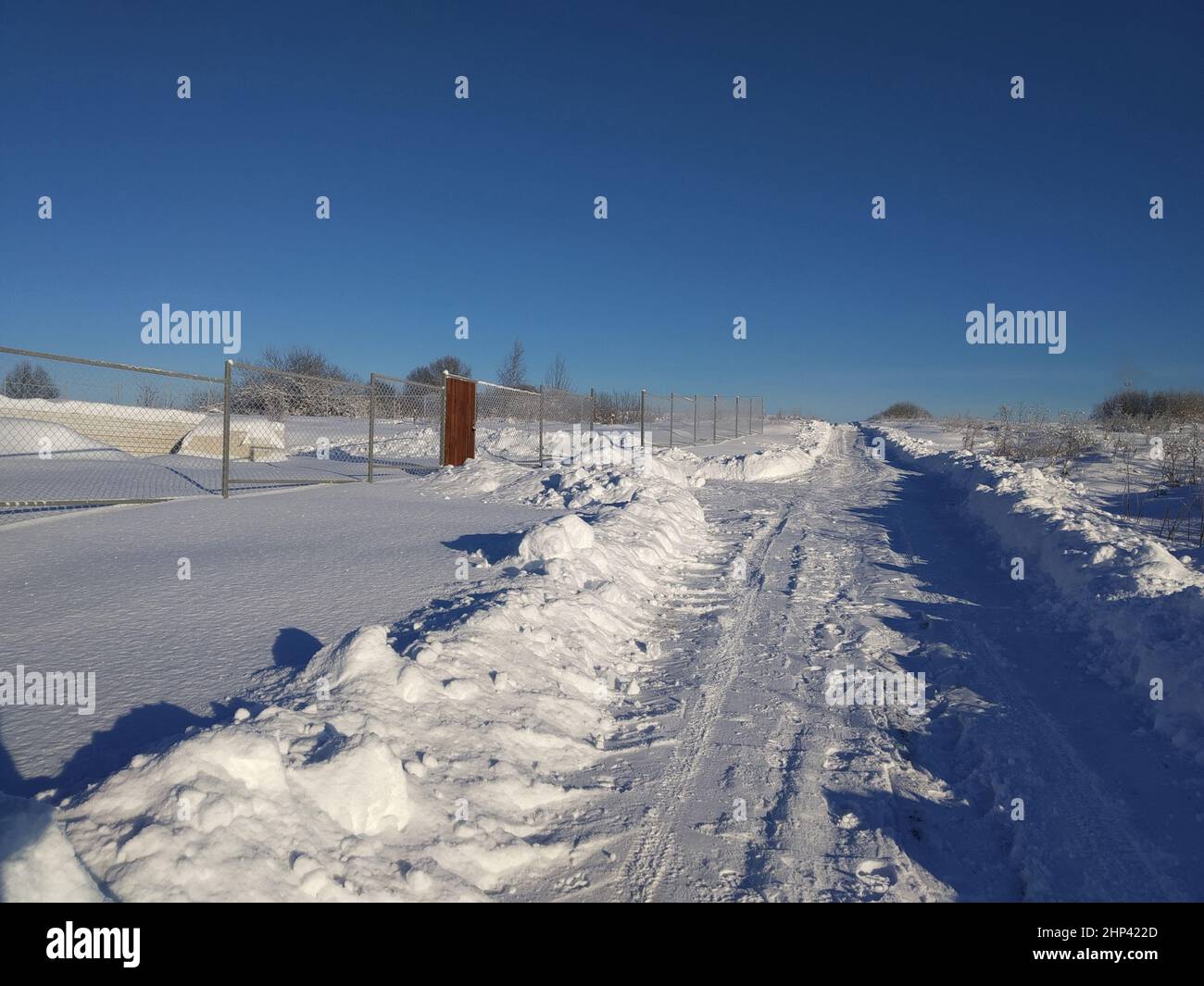 Winter landscape in a Russian village on a sunny day. Snowy road in the countryside against the blue sky Stock Photo