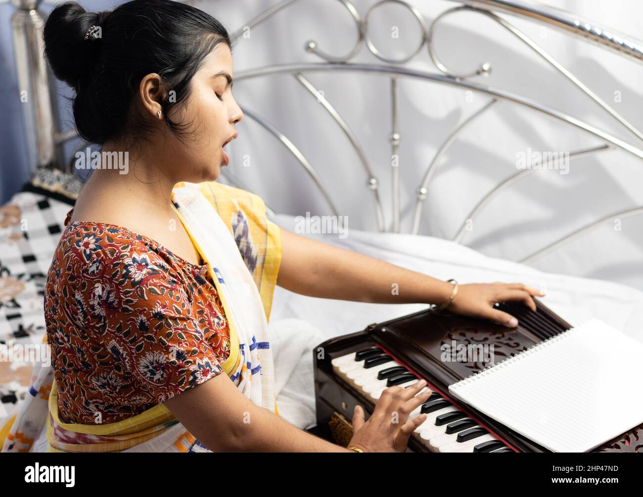 A beautiful Indian woman in saree singing and playing harmonium on white background Stock Photo