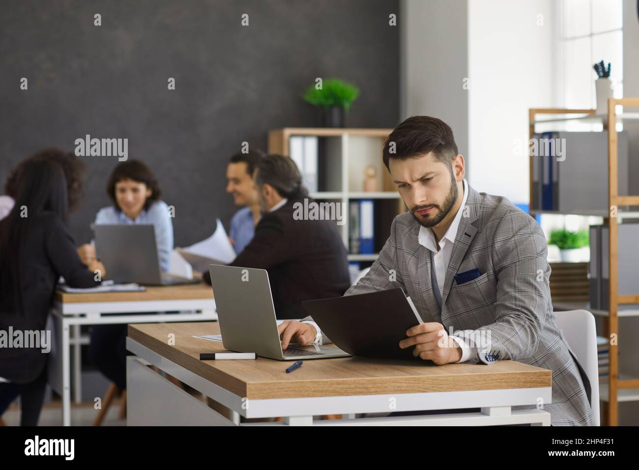 Busy man sits at a table and checks documents while working in a modern bright office. Stock Photo