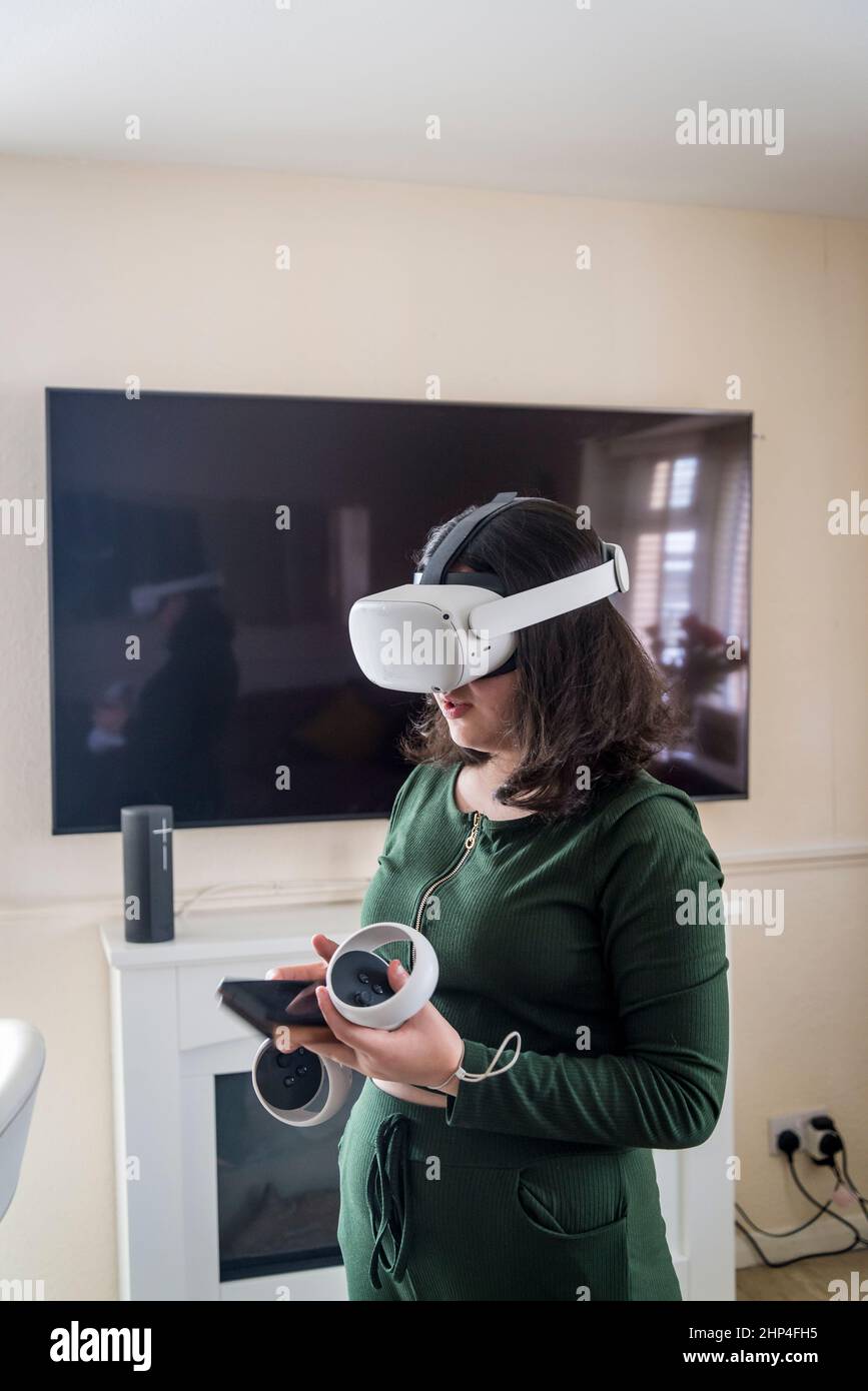 Girl with VR headset and two controllers sitting up her game, London, UK Stock Photo