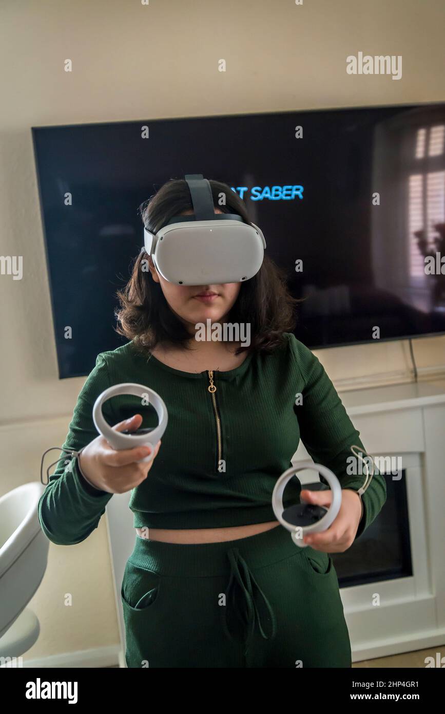 Girl with VR headset and two controllers playing with friends in virtual reality, London, UK Stock Photo