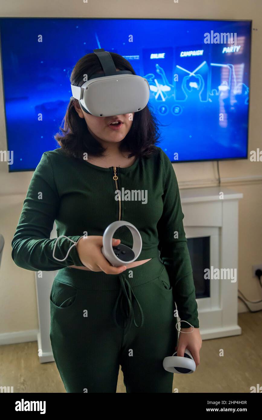 Girl with VR headset and two controllers playing with friends in ...