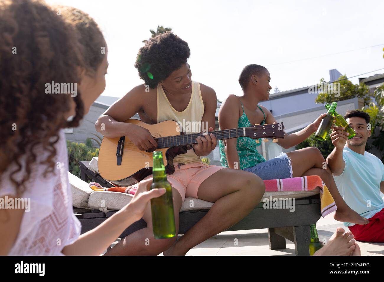 Happy multiracial friends enjoying sunny day at poolside while man playing guitar Stock Photo