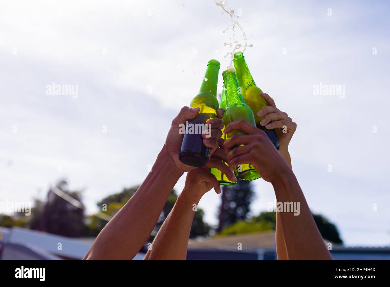 Hands of biracial male and female friends toasting beer bottles against sky Stock Photo
