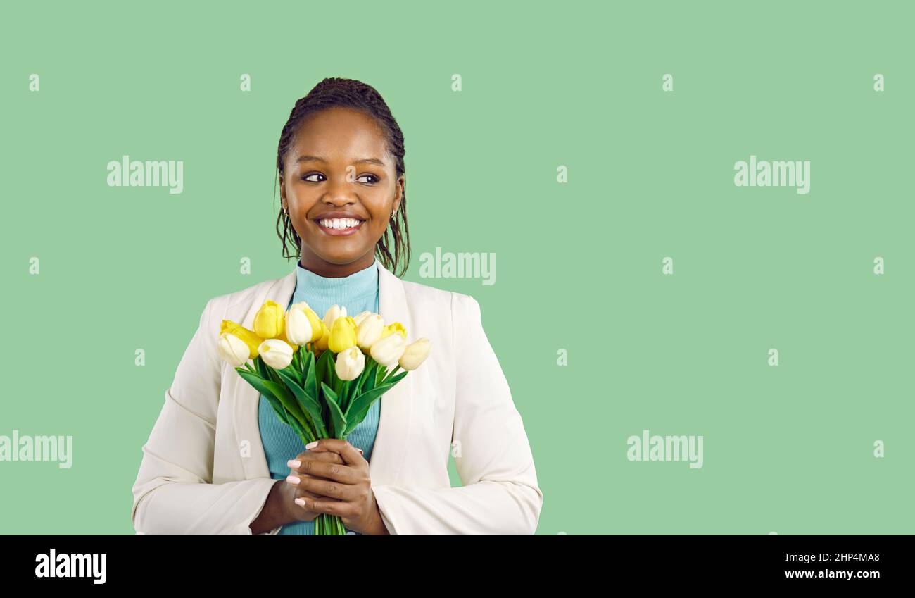 Portrait of beautiful young woman with bouquet of fresh spring tulips on light green background. Stock Photo